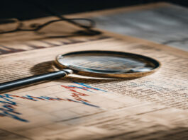 Magnifying glass on a financial newspaper showing stock charts and data