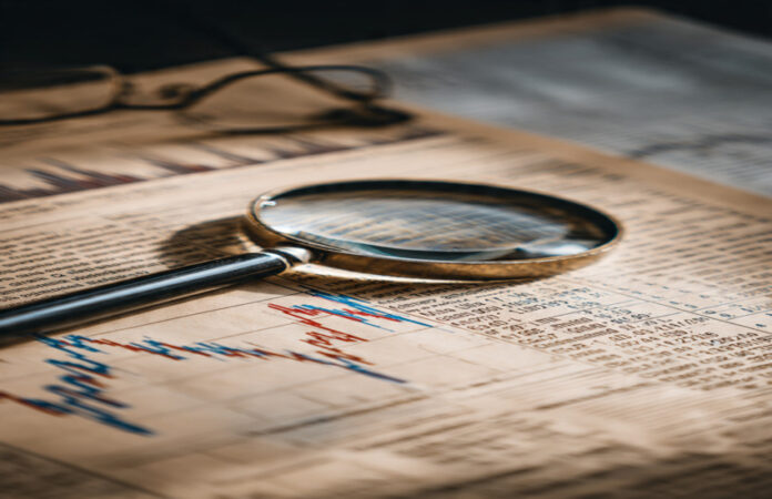 Magnifying glass on a financial newspaper showing stock charts and data