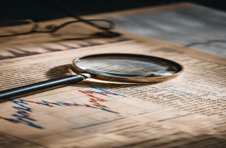 Magnifying glass on a financial newspaper showing stock charts and data